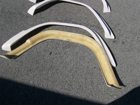 1974 Ford Bronco - Multiple white fender flares are laid out on a dark asphalt surface, with one unpainted fiberglass flare visible.