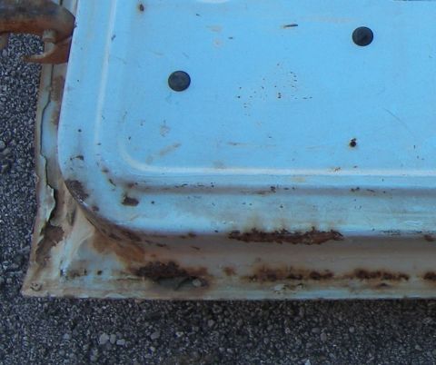 1974 Ford Bronco - Close-up of a light blue door panel showing significant rust damage along its lower section.