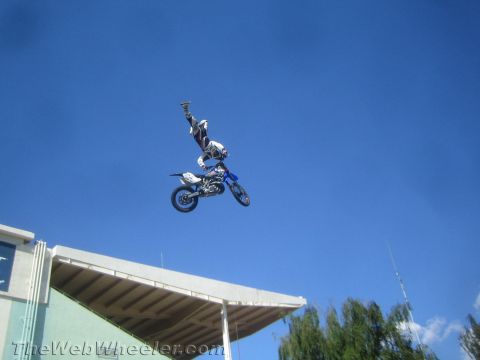 1990 Ford Bronco - freestyle motocross rider tucks into an inverted trick on a blue dirt bike against a clear blue sky.