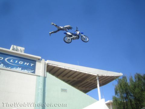 1990 Ford Bronco - motocross rider lies flat behind a blue dirt bike mid-jump over a partial Bud Light sign.