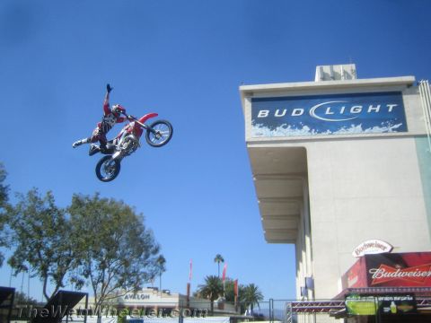 1990 Ford Bronco - freestyle motocross rider performs a kick trick on a red dirt bike beside a large Bud Light building sign.