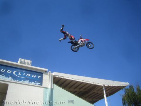 1990 Ford Bronco - motocross rider hangs inverted off a red dirt bike during a high jump above a Bud Light stadium sign.