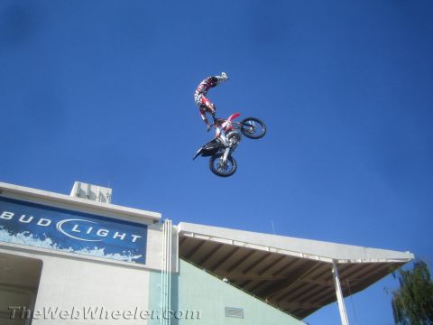 1990 Ford Bronco - motocross rider goes nose-up in a kiss-of-death-style trick on a red dirt bike above a Bud Light sign.