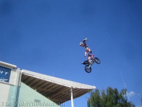 1990 Ford Bronco - Two freestyle motocross riders perform synchronized tricks on dirt bikes high above a stadium roof.