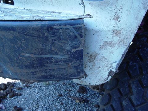 1985 Ford Bronco - Close-up of a muddy vehicle fender and tire, with gravel on the ground.