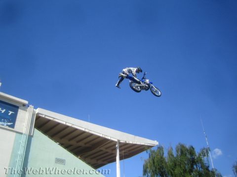 1990 Ford Bronco - motocross rider hangs inverted over a blue dirt bike mid-jump beside a partial Bud Light sign.