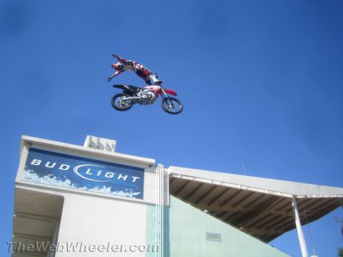 1990 Ford Bronco - freestyle motocross rider performs an extended trick over the seat of a red and white dirt bike high above a Bud Light stadium sign.