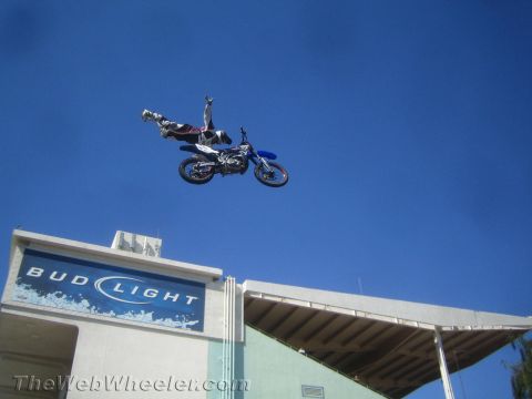 1990 Ford Bronco - motocross rider hangs nearly upside down above a blue dirt bike during a freestyle jump over a stadium with a Bud Light sign.
