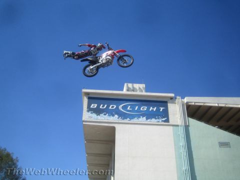 1990 Ford Bronco - freestyle motocross rider extends sideways over a red and white dirt bike high above a Bud Light stadium sign and blue sky.