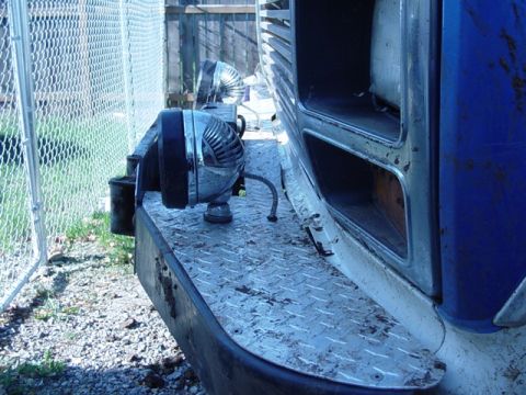 1985 Ford Bronco - Chrome spotlight and siren-style auxiliary lights mounted on a diamond-plate front bumper of a blue truck by a fence.