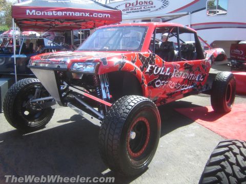 1990 Ford Bronco - red tube-chassis off-road buggy lettered Full Potential Offroad with long-travel suspension sits on display under vendor tents.