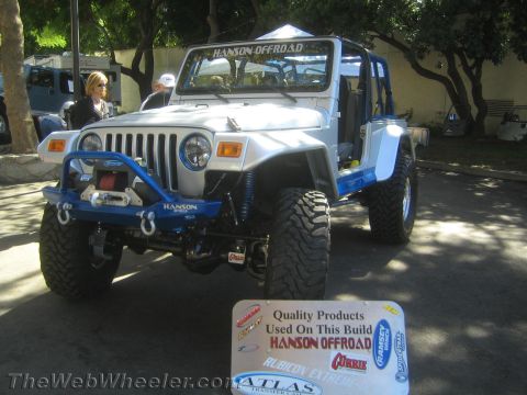 1990 Ford Bronco - silver lifted Jeep Wrangler with a Hanson Offroad winch bumper and blue accents sits on display beside a product placard at a show.