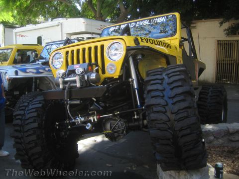 1990 Ford Bronco - yellow Jeep-based rock crawler lettered Off Road Evolution sits on huge mud tires with a winch bumper at an outdoor show.