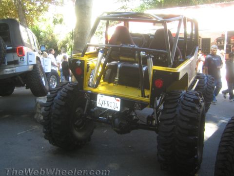 1990 Ford Bronco - rear of a yellow tube-chassis Jeep rock crawler shows the cage, fuel cells and a California license plate at a crowded show.