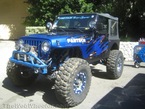 1990 Ford Bronco - blue lifted Jeep Wrangler with Fabtech Motorsports graphics, beadlock wheels and mud tires sits on display at an outdoor show.