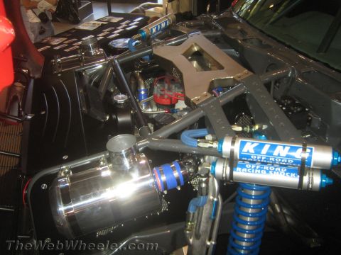 1990 Ford Bronco - Close-up of chrome and blue King off-road racing shocks with a reservoir mounted in a custom off-road vehicle's engine bay.