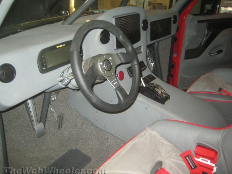 1990 Ford Bronco - Custom gray vinyl interior of an off-road vehicle showing a black racing steering wheel, floor shifter, pedals, and red seat trim.