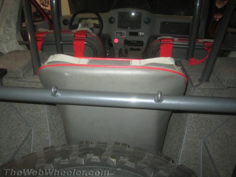 1990 Ford Bronco - Interior of a custom off-road vehicle showing a gray rear bench seat with red harness straps facing the dashboard and steering wheel.