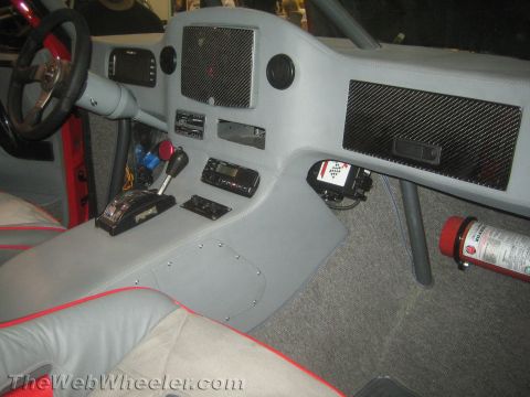 1990 Ford Bronco - Custom gray dashboard of an off-road vehicle with carbon-fiber-look vents, a floor shifter, electronics, and a mounted fire extinguisher.
