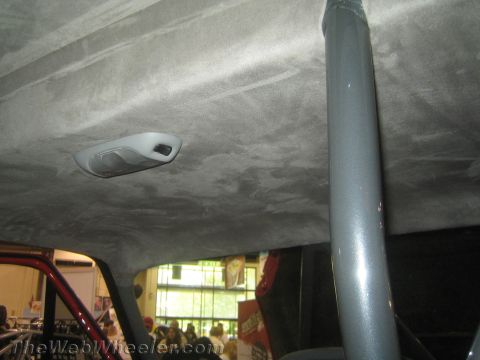 1990 Ford Bronco - Interior ceiling of an off-road vehicle showing a gray suede headliner, a dome light, and a roll cage tube running through.