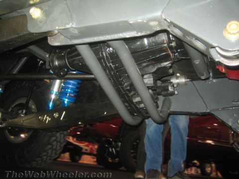 1990 Ford Bronco - Underbody close-up of an off-road vehicle showing the transfer case, driveshafts, skid plates, and a blue coilover shock.
