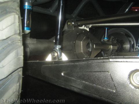 1990 Ford Bronco - Underbody close-up of an off-road vehicle's front axle and differential with blue bypass shocks and a skid plate.