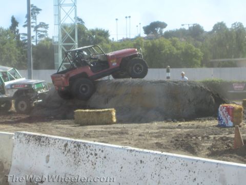 1990 Ford Bronco - Red tube-bodied Jeep off-road buggy cresting a large dirt mound while a yellow Jeep waits at left on the competition course.