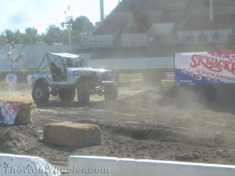 1990 Ford Bronco - White lifted tube-bodied Jeep buggy kicking up dust on a dirt course beside a large Skyjacker sponsor banner.