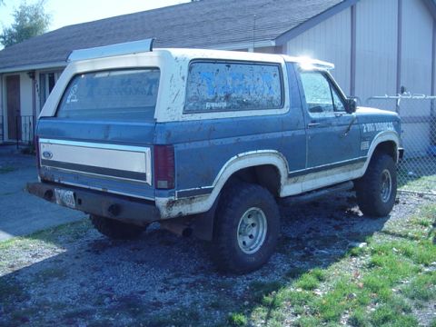 1985 Ford Bronco - This Ford Bronco is parked in a gravel driveway next to a house and a chain-link fence.