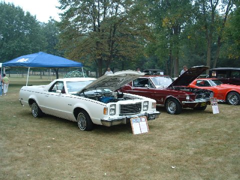 1973 Ford Ranchero - A white 1973 Ford Ranchero is displayed with its hood open, alongside other classic cars on a grassy field.