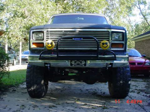 1984 Ford Bronco - This lifted Ford Bronco is parked in a driveway with a red car visible behind it.