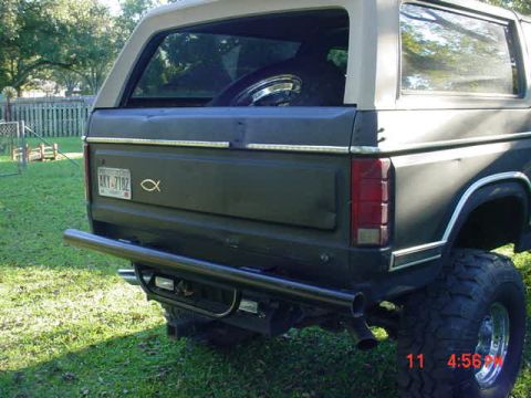 1984 Ford Bronco - Rear view of a 1984 Ford Bronco with an aftermarket bumper and spare tire visible through the window.
