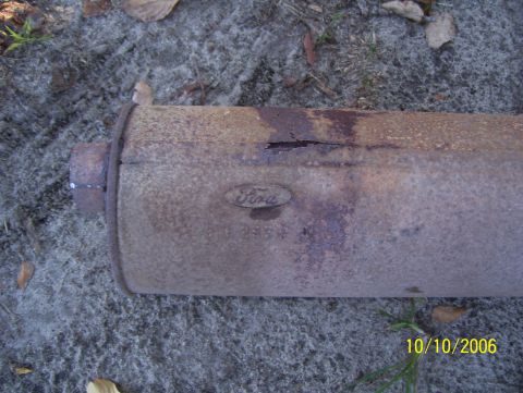 1978 Ford Bronco - A rusty Ford exhaust muffler lies on the ground, showing a Ford oval logo and some part numbers.