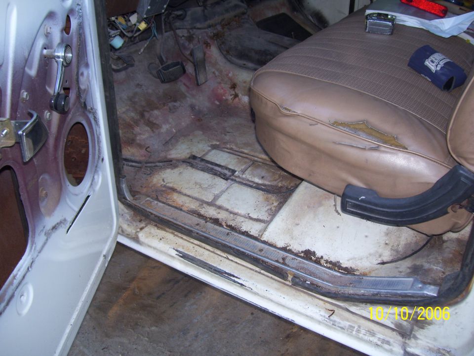 Gutted Ford truck interior with bare rusty floor pan, exposed pedals and torn tan bench seat