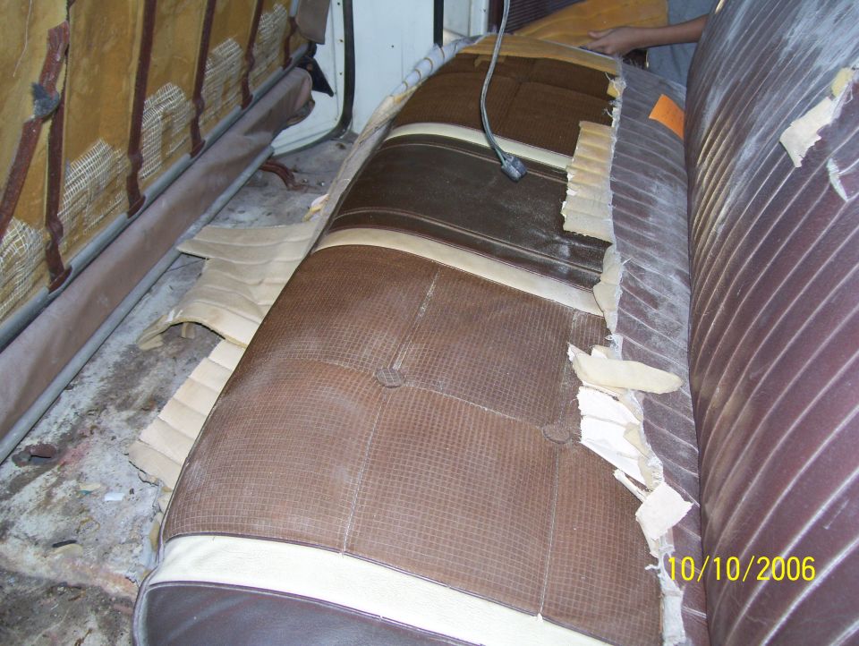 Brown bench seat being reupholstered, vinyl cover torn away exposing padding