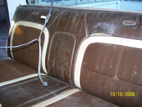 1978 Ford Bronco - Weathered brown and cream 1970s bench seat removed from a vehicle and sitting outdoors, with mildewed vinyl bolsters, tufted brown cloth in…