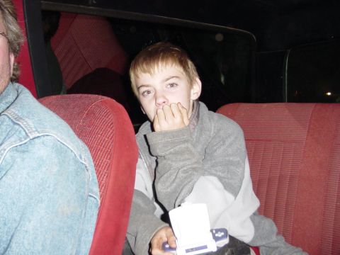 1985 Ford Bronco - A young boy sits in the back seat of a vehicle, looking towards the camera with his hand near his mouth.