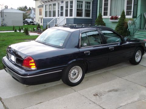 2000 Ford Crown Victoria - A dark blue sedan is parked in front of a house, viewed from the rear quarter.