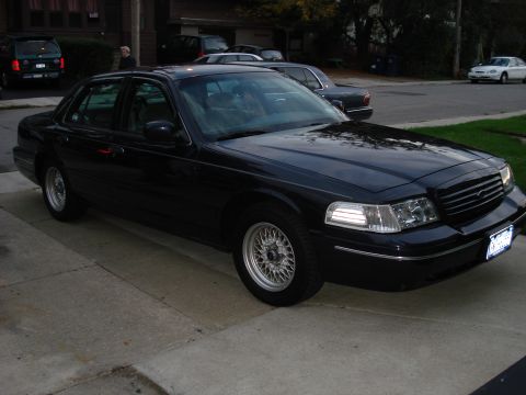 2000 Ford Crown Victoria - A black 2000 Ford Crown Victoria sedan is parked on a driveway, viewed from the front three-quarter angle.