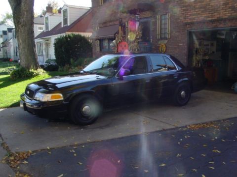 2003 Ford Crown Victoria - A black sedan is parked in a driveway in front of a house and an open garage.