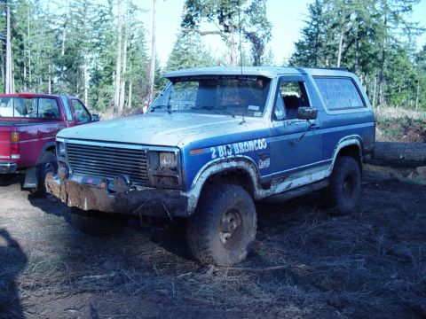 1985 Ford Bronco - A blue Ford Bronco sits in a muddy outdoor area next to a red pickup truck.