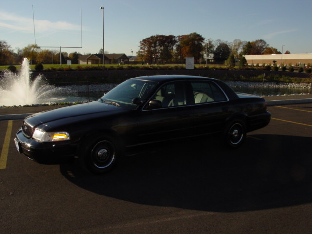 Black 2003 Ford Crown Victoria parked in a lot with a fountain and football goalposts in the background