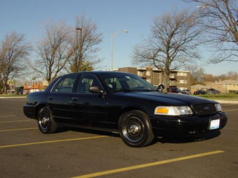 2003 Ford Crown Victoria - A black 2003 Ford Crown Victoria is parked in an empty lot under a clear sky.