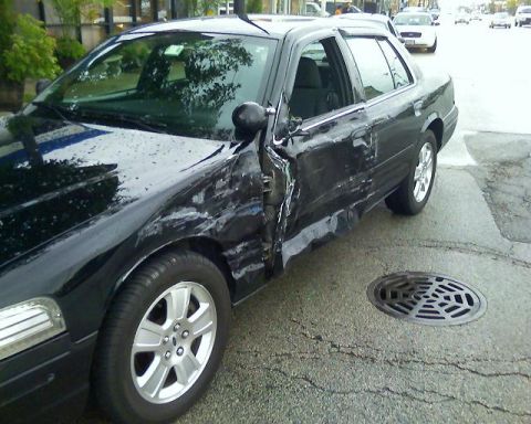2003 Ford Crown Victoria - A black 2003 Ford Crown Victoria shows significant damage to its driver's side door and fender.