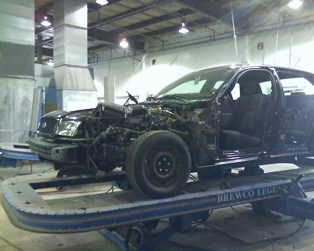 Black 2003 Ford Crown Victoria with front end disassembled on a repair lift
