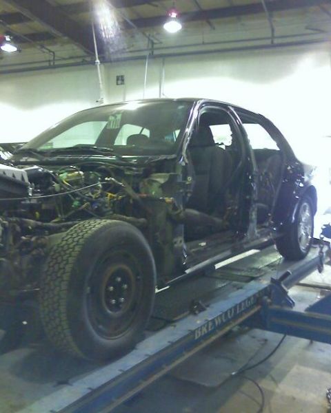2003 Ford Crown Victoria - A damaged car is shown on a lift in a repair shop, with its engine and interior exposed.