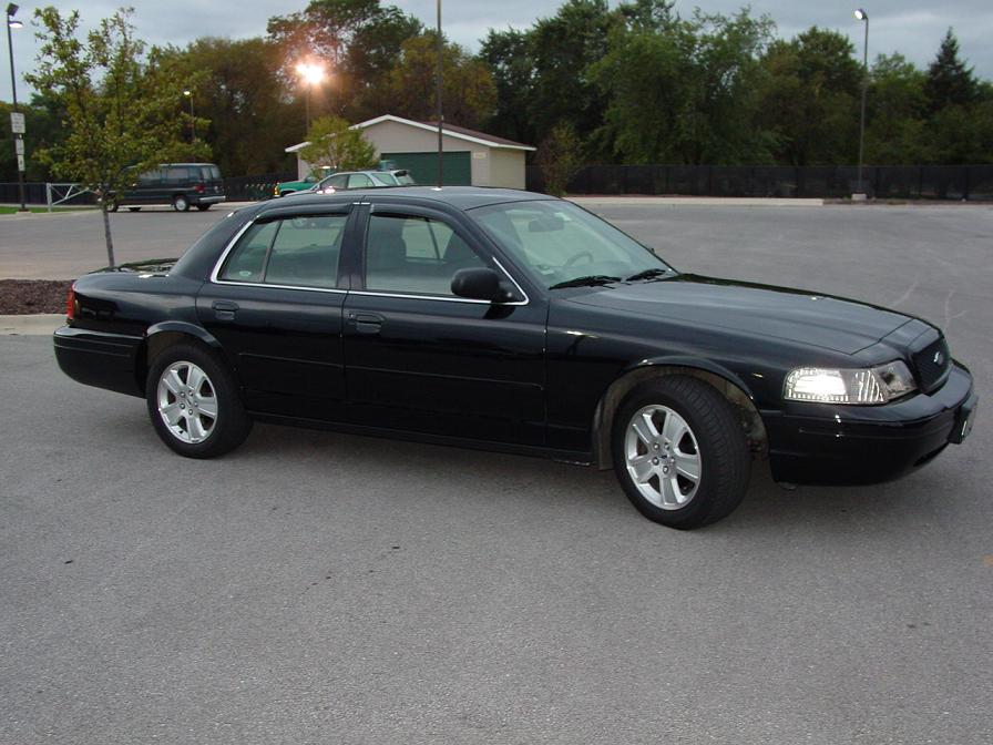 Black full-size Ford Crown Victoria sedan parked in an empty lot at dusk