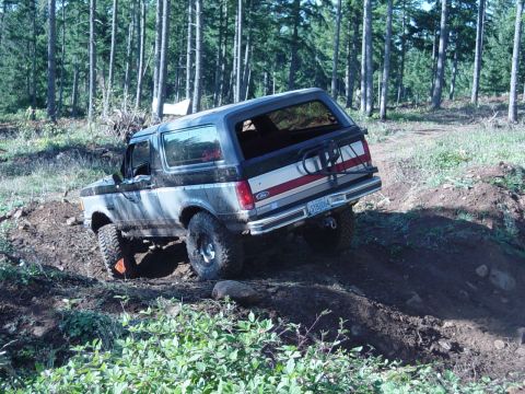 1985 Ford Bronco - This Ford Bronco is navigating a steep, muddy incline on a wooded trail.