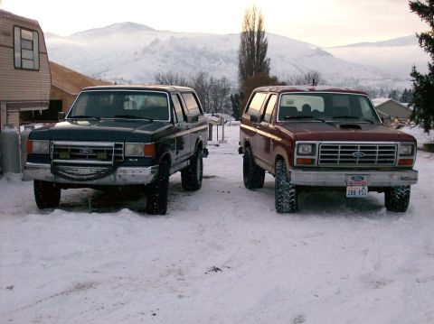1988 Ford Bronco - Two Ford Broncos are parked in a snowy landscape with mountains visible in the distance.