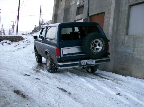1988 Ford Bronco - This SUV, likely from the 1980s, is parked on a snow-covered road next to a concrete building.